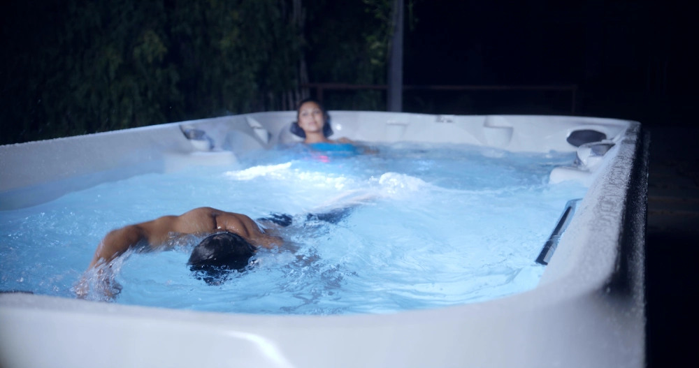 are swim spas worth it? couple enjoying their swim spa. man is swimming and woman is enjoying a hydromassage